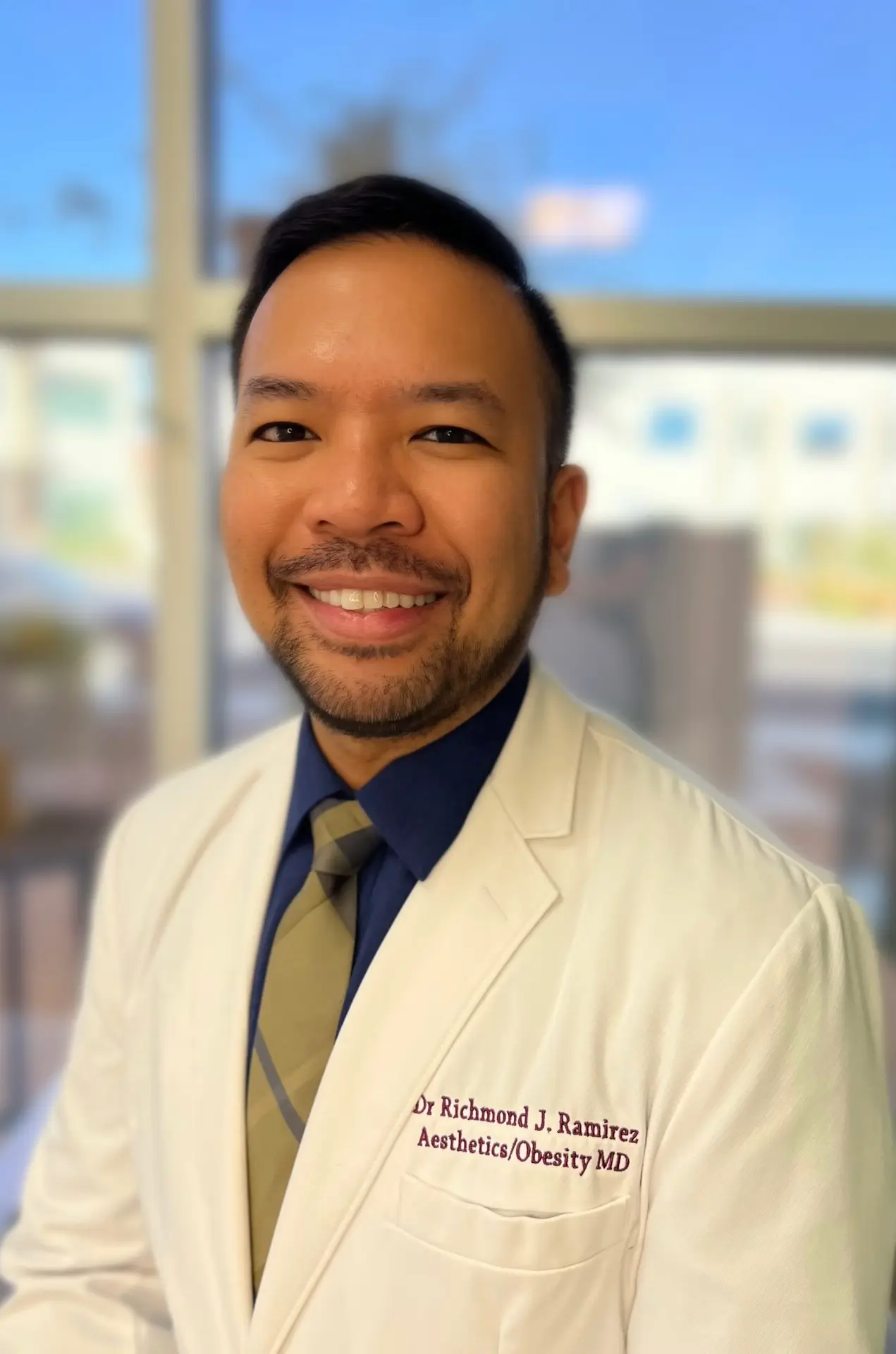 Richmond Ramirez, MD, in his clinic, wearing a coat embroidered 'Dr Richmond J. Ramirez, Aesthetics/Obesity MD'